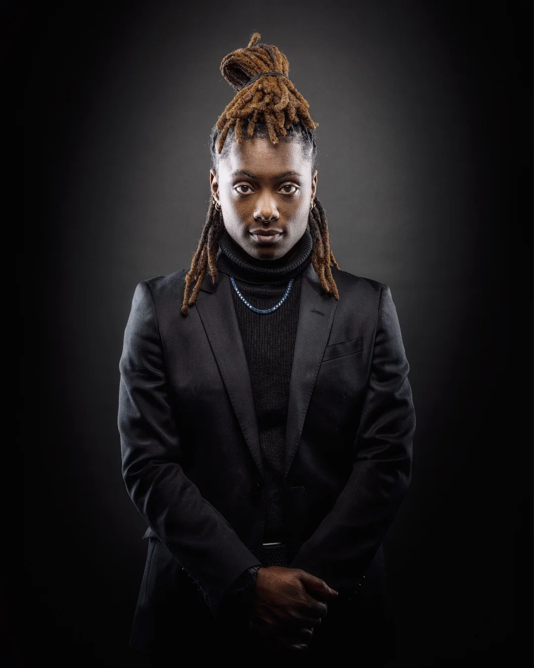 Portrait of Roseyanna The Poet in a black suit against a dark background